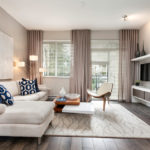 Dzīvojamās istabas dekors gaiši smilškrāsā ar dīvānu un horizontālām žalūzijām uz logiem.