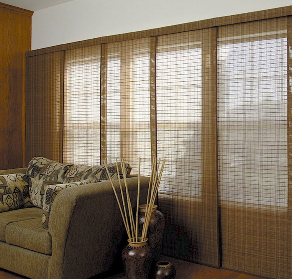 Bīdāmie bambusa aizkari uz viesistabas loga aiz dīvāna