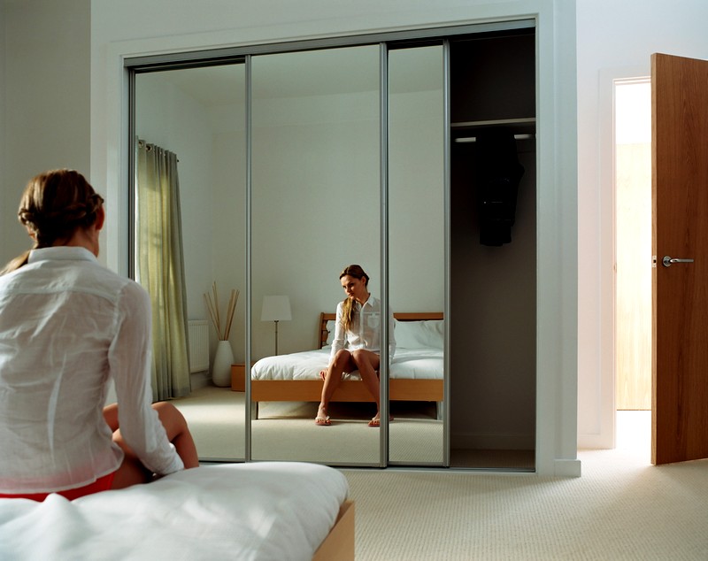 Reflectarea unei fete într-un dulap cu oglinzi dintr-un dormitor