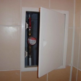 Compteur d'eau derrière la porte entrouverte de la trappe de plomberie
