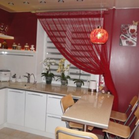 Sarkans aizkars uz virtuves loga ar baltām mēbelēm