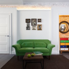 Zaļš dīvāns pie viesistabas baltas sienas